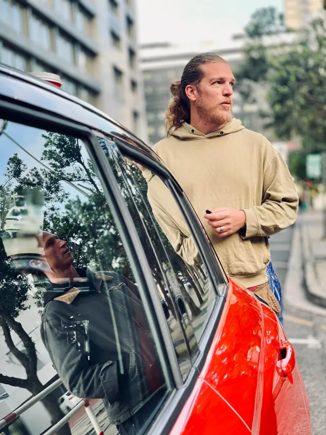 Talent beside a red car on a city street